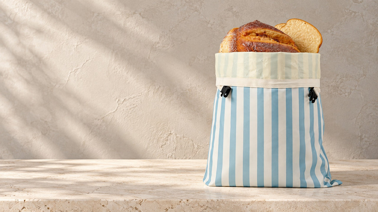 Striped beeswax bread bag holding a sourdough loaf on limestone