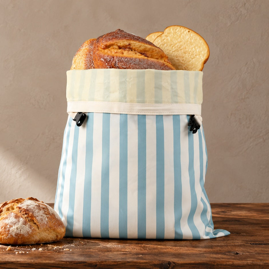 Beeswax bread bag in Coastal Blue stripe holding a sourdough loaf on a walnut table